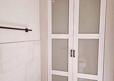 Modern bathroom with white double doors, glass panels, and a sleek design, showcasing renovation expertise by NorthWest Granite & Flooring LLC.