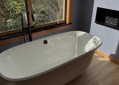 Modern freestanding bathtub in a well-lit bathroom, featuring large windows and elegant wood accents, showcasing NorthWest Granite & Flooring LLC's bathroom renovation expertise.