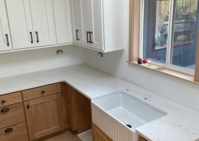 Modern kitchen remodel featuring white cabinetry, quartz countertops, and a farmhouse sink, showcasing NorthWest Granite & Flooring LLC's renovation expertise.