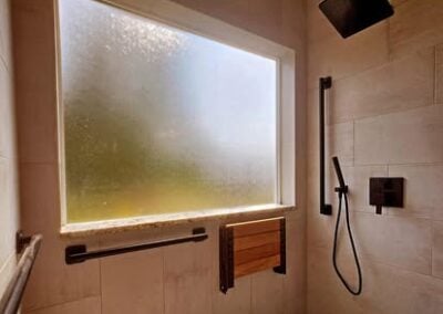 Modern shower remodel featuring a frosted window, sleek black fixtures, and a wooden bench, showcasing NorthWest Granite & Flooring LLC's expertise in bathroom renovations.