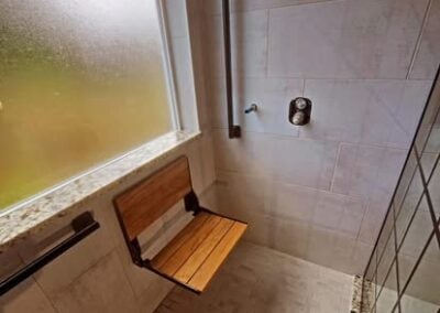 Shower remodel featuring a wooden seat, modern fixtures, and natural light from a frosted window, showcasing NorthWest Granite & Flooring LLC's bathroom renovation expertise.